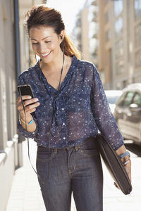 Happy businesswoman listening music through mobile phone on sidewalk