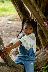 Portrait of smiling girl sitting on tree trunk