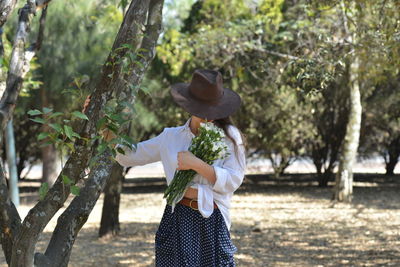 Midsection of woman wearing hat standing by tree