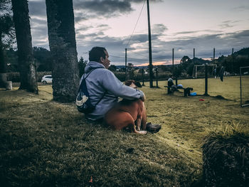 Rear view of man sitting on field against sky