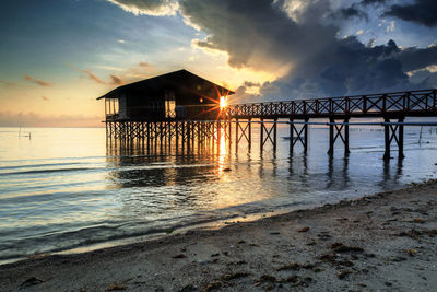 Silhouette built structure on beach against sky during sunset