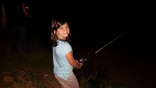 Portrait of girl holding fishing rod at night