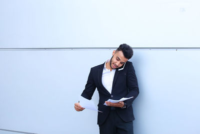 Young businessman reading document while talking on phone