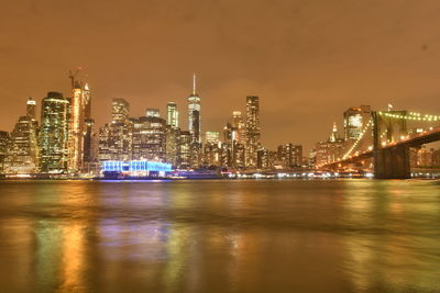 Illuminated modern buildings by river against sky at night