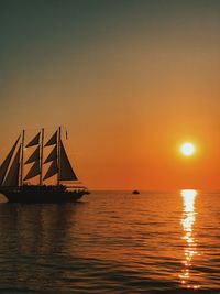 Silhouette sailboat in sea against orange sky