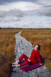 Woman  in red warm clothes and a big scarf on an ecological trail in the autumn not a swamp