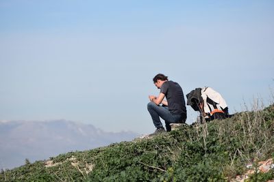 Low angle view of man sitting on rock over hill against sky