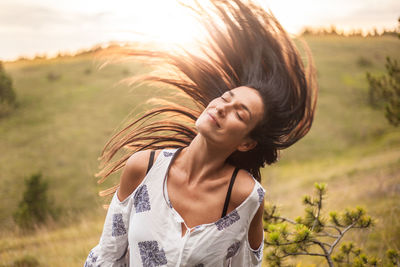 Beautiful young woman tossing hair while standing on field