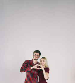 Portrait of young couple making heart shape standing against wall