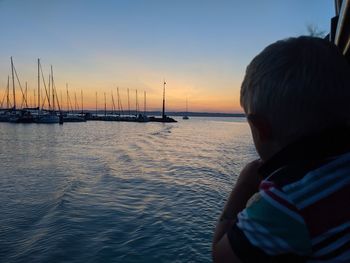 Rear view of boy on sailboat at sea against sky