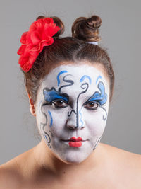 Close-up portrait of woman with face paint against gray background