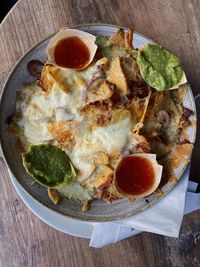 High angle view of cheesy nachos with guacamole in plate on table