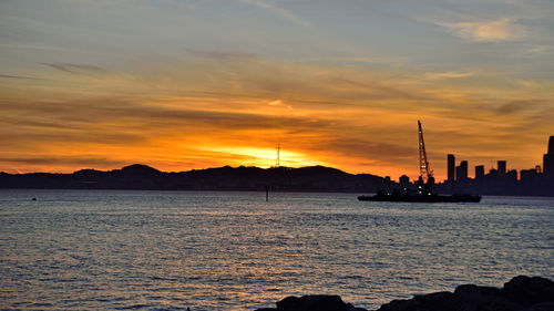 Silhouette sailboats in sea against orange sky