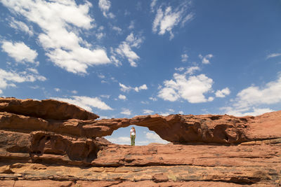 Woman looking up while standing on rock formation against sky