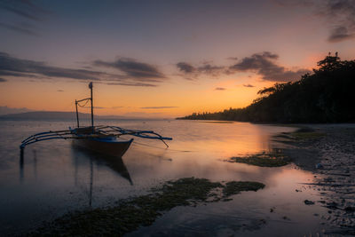 Boat moored in sea against sky during sunset