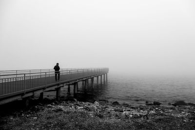 Man standing on railing by sea against sky