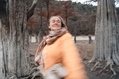 Woman standing by tree trunk in forest
