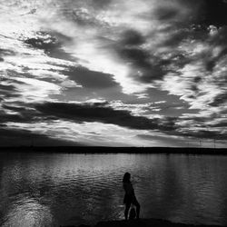 Silhouette people on calm lake against cloudy sky