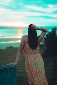Rear view of woman with hand in hair looking at sea during sunset