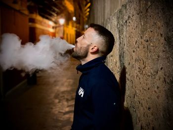 Side view of young man standing against wall