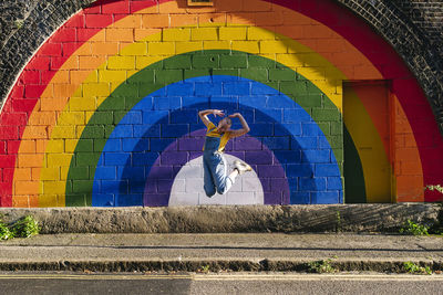 Cheerful transgender person jumping in front of rainbow wall