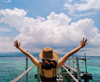 Rear view of woman with arms outstretched standing over sea against sky