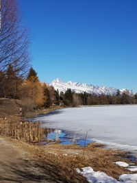 Scenic view of lake by snowcapped mountains against clear blue sky