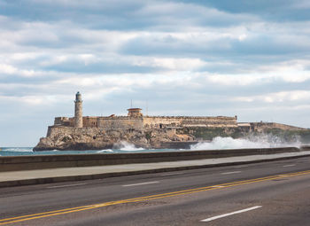 Road by sea against cloudy sky