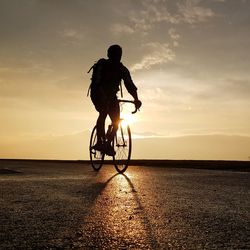 Silhouette man riding bicycle at beach during sunset