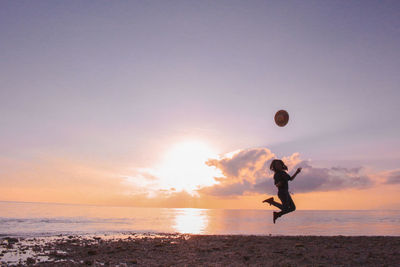 Silhouette woman jumping with hat in mid-air at beach