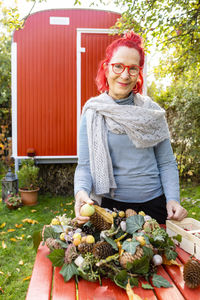 Portrait of smiling senior woman with red dyed hair tinkering autumnal decoration in the garden