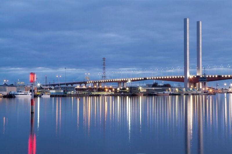 ILLUMINATED BRIDGE OVER SEA AGAINST SKY