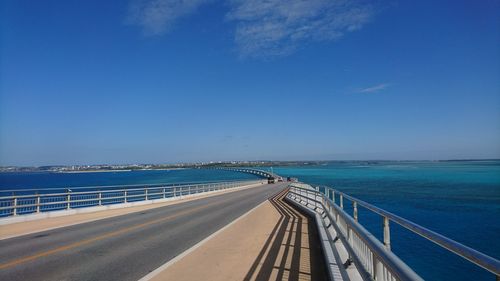 View of road by sea against blue sky