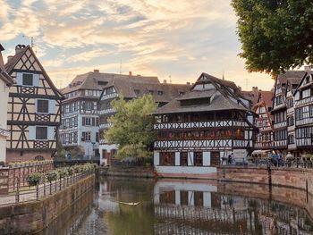 Buildings by river against sky during sunset