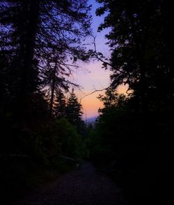 Road amidst silhouette trees in forest against sky