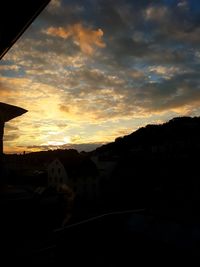 Silhouette houses against cloudy sky at sunset