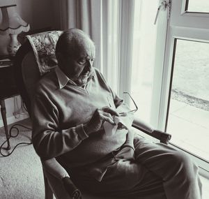 High angle view of senior man cleaning eyeglasses while sitting on armchair