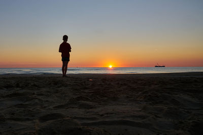 Silhouette man standing on beach against sky during sunset