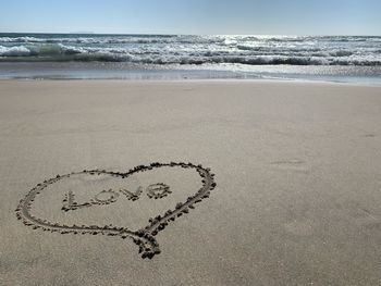 Heart shape and the word love on sand at beach against sky