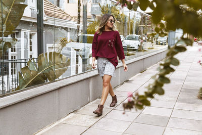 Young woman walking on sidewalk by glass building