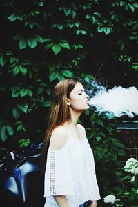 Woman exhaling smoke against trees