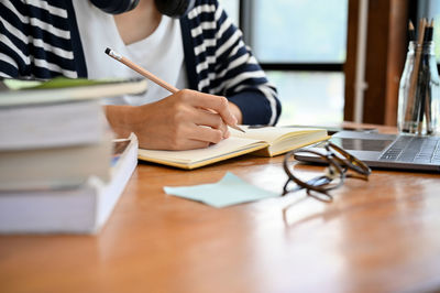 Midsection of woman writing in book at table