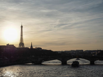 Bridge over river by buildings against sky during sunset