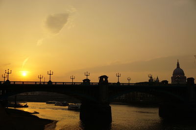Silhouette bridge over river against sky during sunset