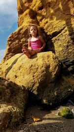 Low angle portrait of girl sitting on rock