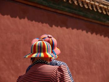 Rear view of woman and men wearing hat against wall