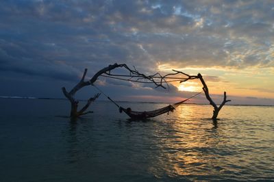 Silhouette bare tree by sea against sky during sunset