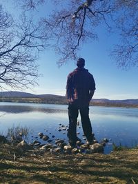 Rear view of man standing by lake against sky