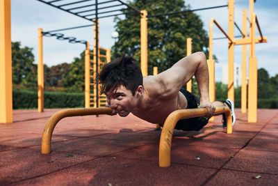 Young shirtless man bodybuilder doing push-ups on a parallel bars during his workout