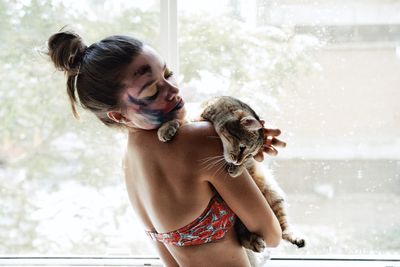 Woman holding cat against window at home